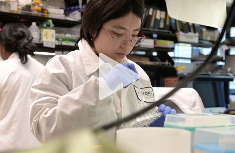 Woman working in a lab at Gladstone Institutes with a transparent play button overlaid.