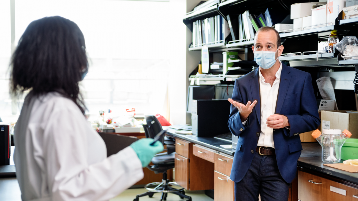 Leor Weinberger wearing a mask in the lab talking to another scientist