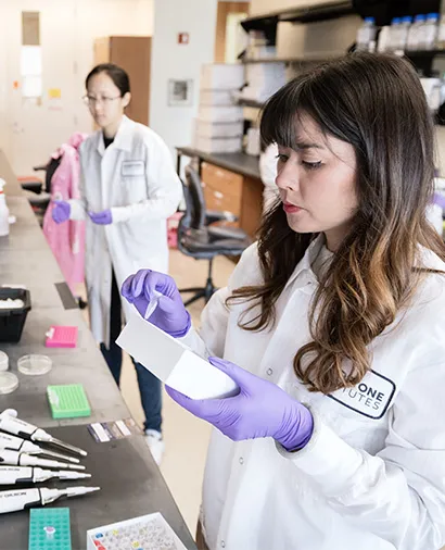 Scientist Kim Dam in a lab coat and gloves working at a lab bench
