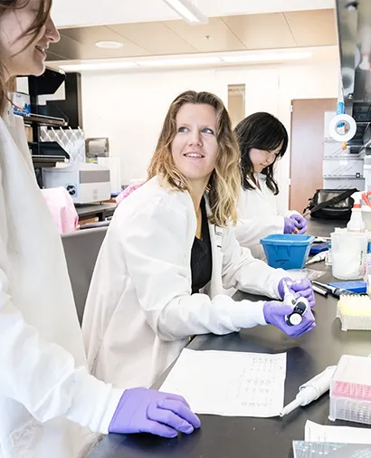 Scientists in lab coats and gloves working together at a lab bench