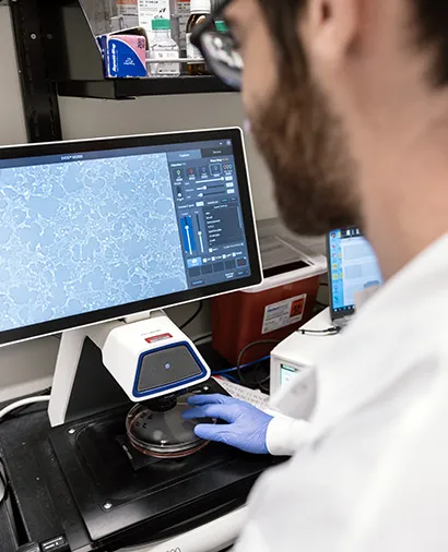 Side of a scientist in a lab coat standing in front of a screen looking a scientific image