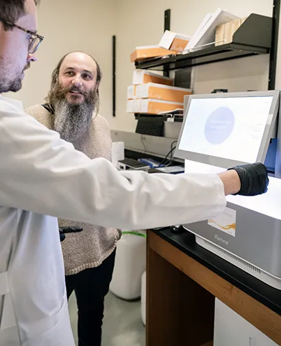 Seth shipman looking at another scientist while that scientist is looking at a screen of a piece of lab equipment