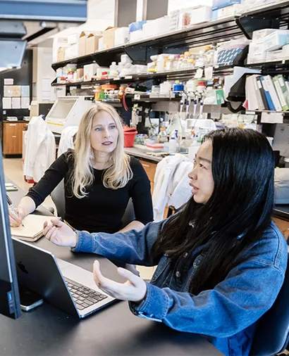 Julia Carnevale talking to another scientist sitting at a lab bench working with a laptop
