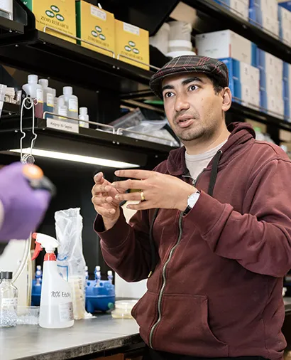Sukrit Silas talking to someone in the lab with his hands forming a circle