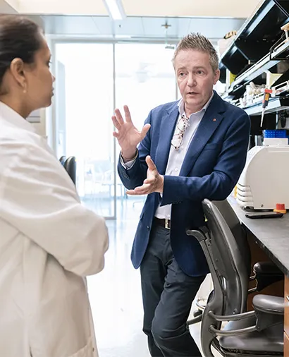 Benoit Bruneau leaning against a chair talking to another scientist in the lab