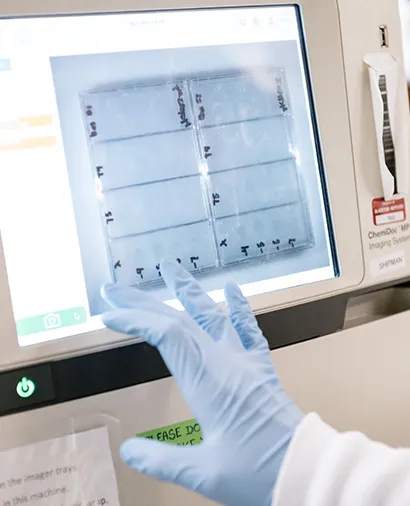 Close up of a screen on a piece of lab equipment with a gloved hand touching the screen