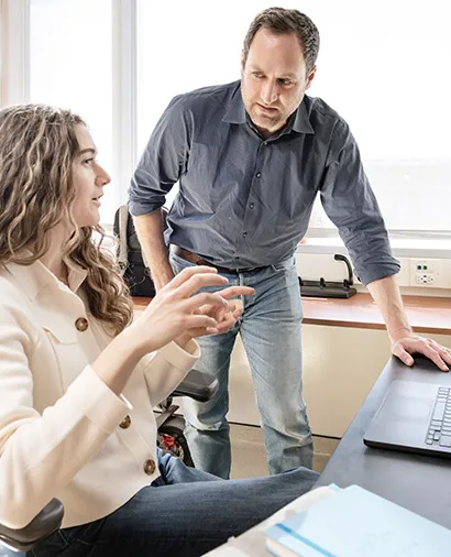 Alex Marson standing at a lab bench talking to another scientist sitting at the bench