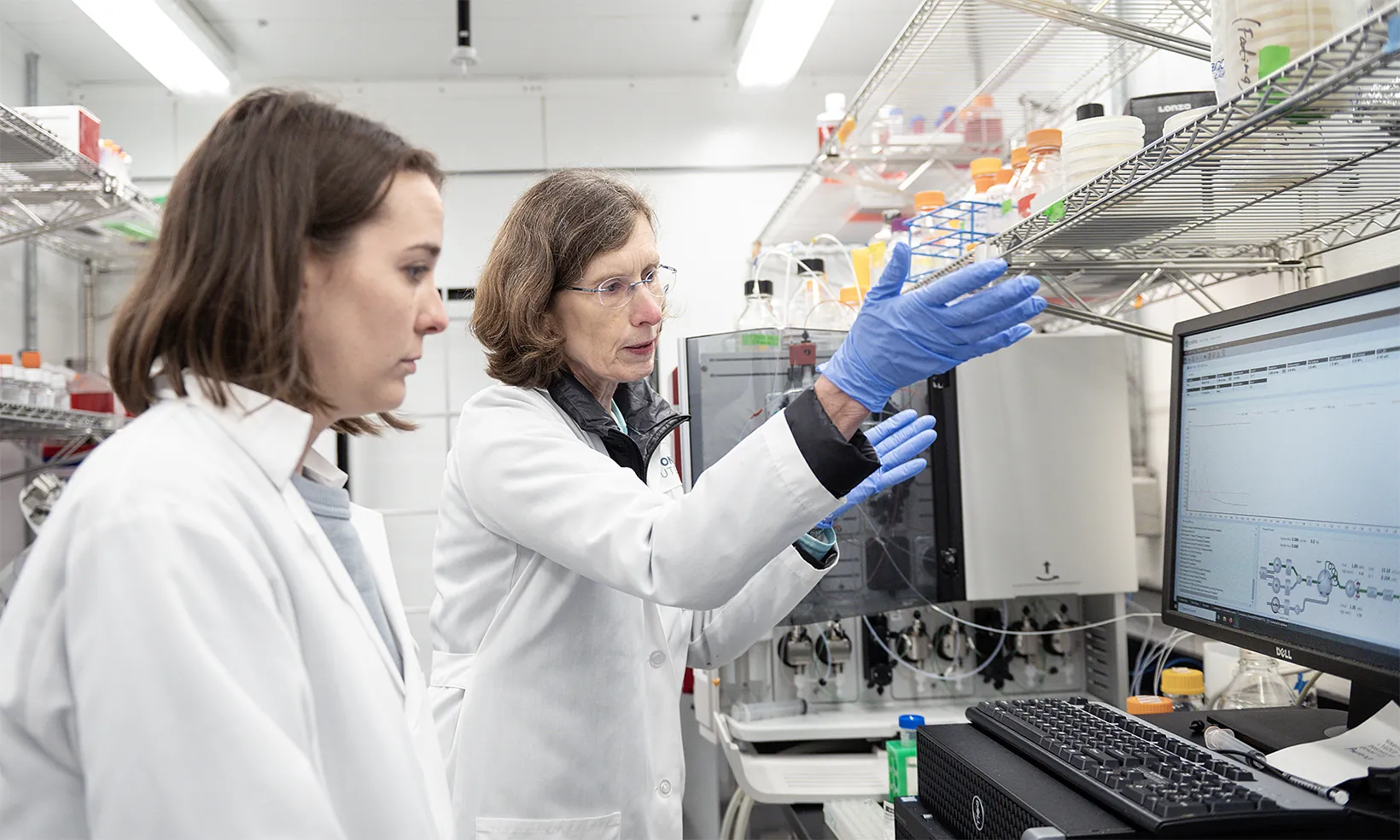 Two scientists in lab coats working at a computer screen in the lab
