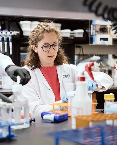 A scientist in a red shirt and lab coat working at the lab bench