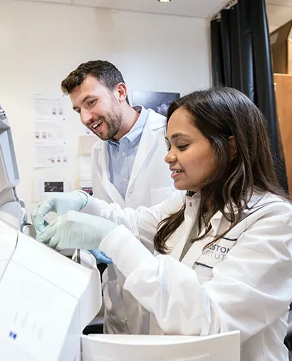 Two scientists standing, working with some lab equipment