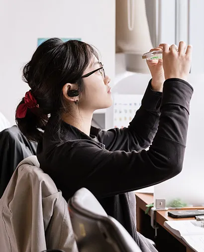 Scientist holding up a dish, studying it, while sitting at a lab bench