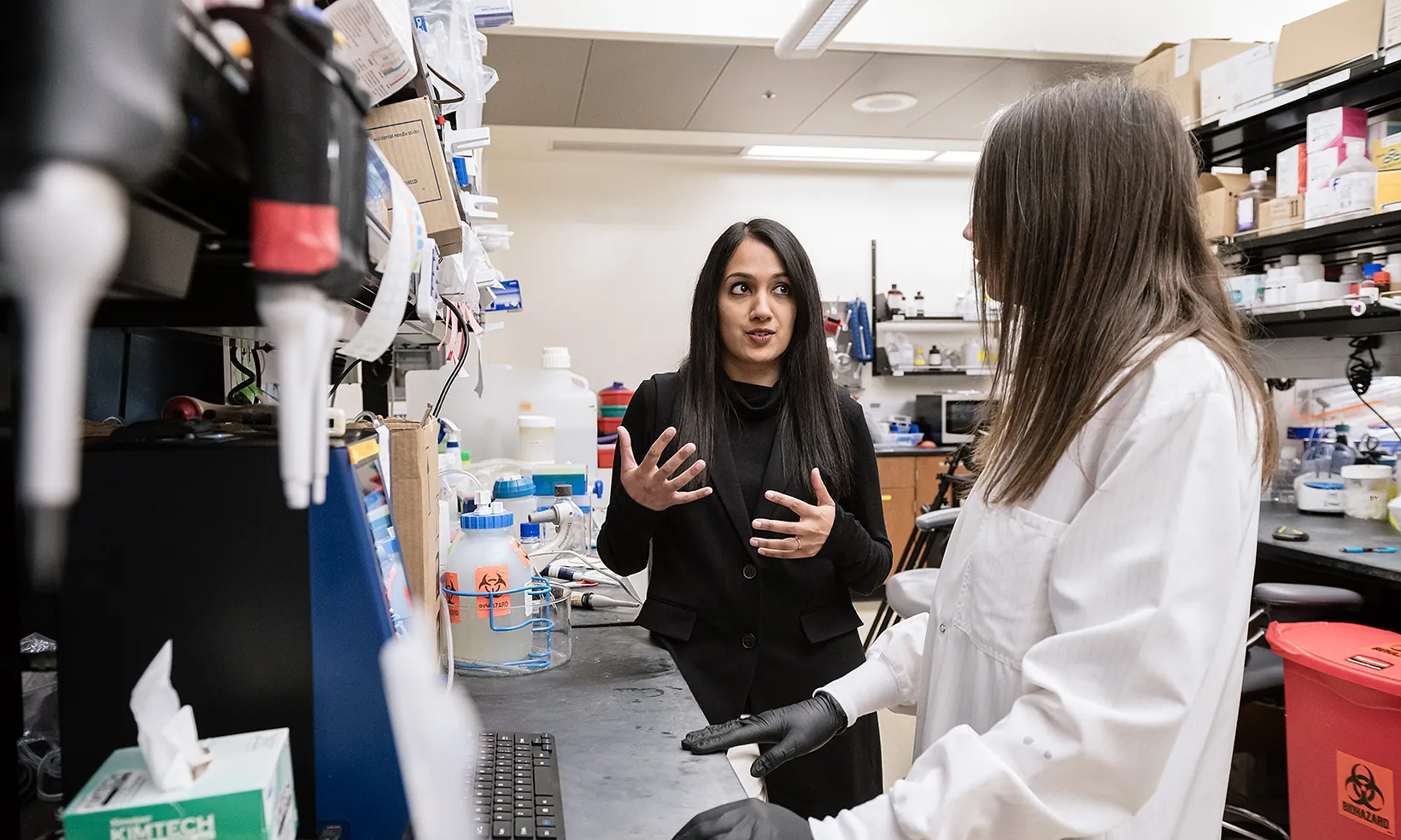 Isha Jain standing at a lab bench talking to another scientist in a lab coat