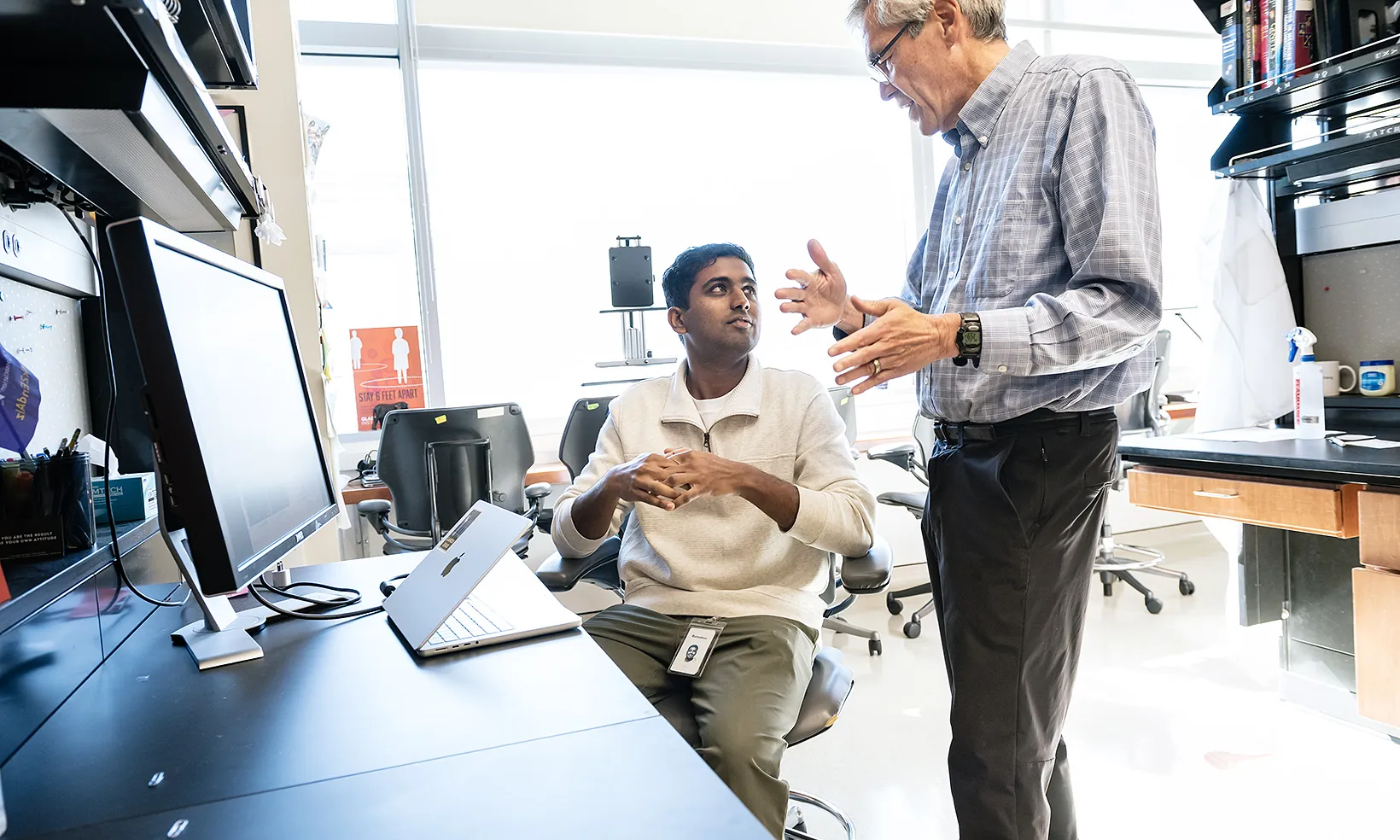 Bruce Conklin standing at a lab bench, talking to another scientist who is sitting down